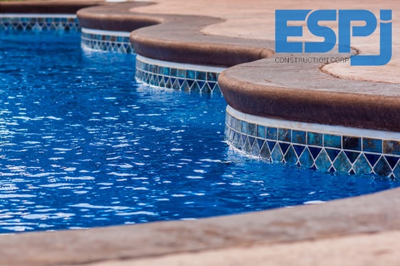 Curved pool coping wall with a zigzag stone cap and blue mosaic tile accent